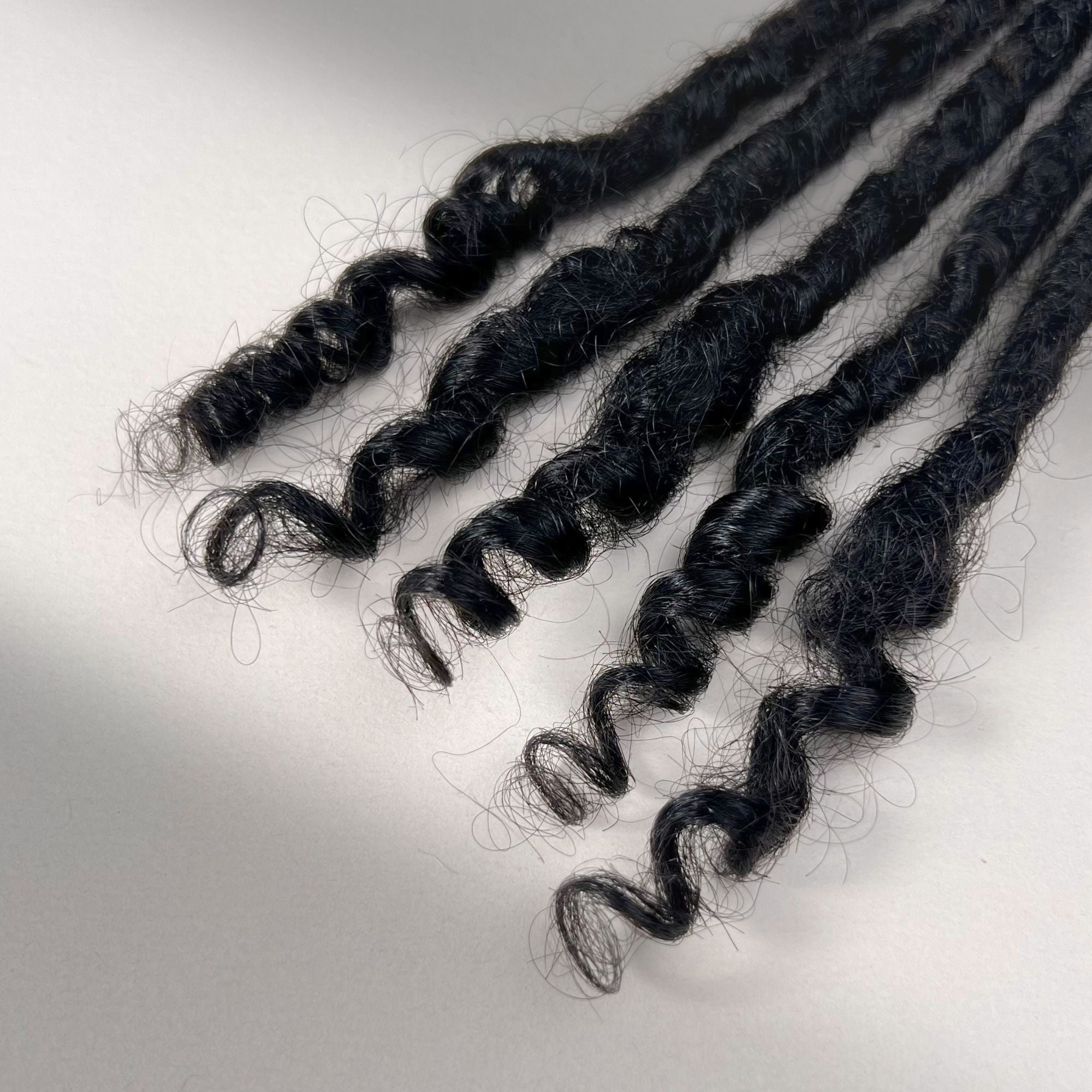 Tip detail of kinky loc extensions with curly ends in Natural Black.