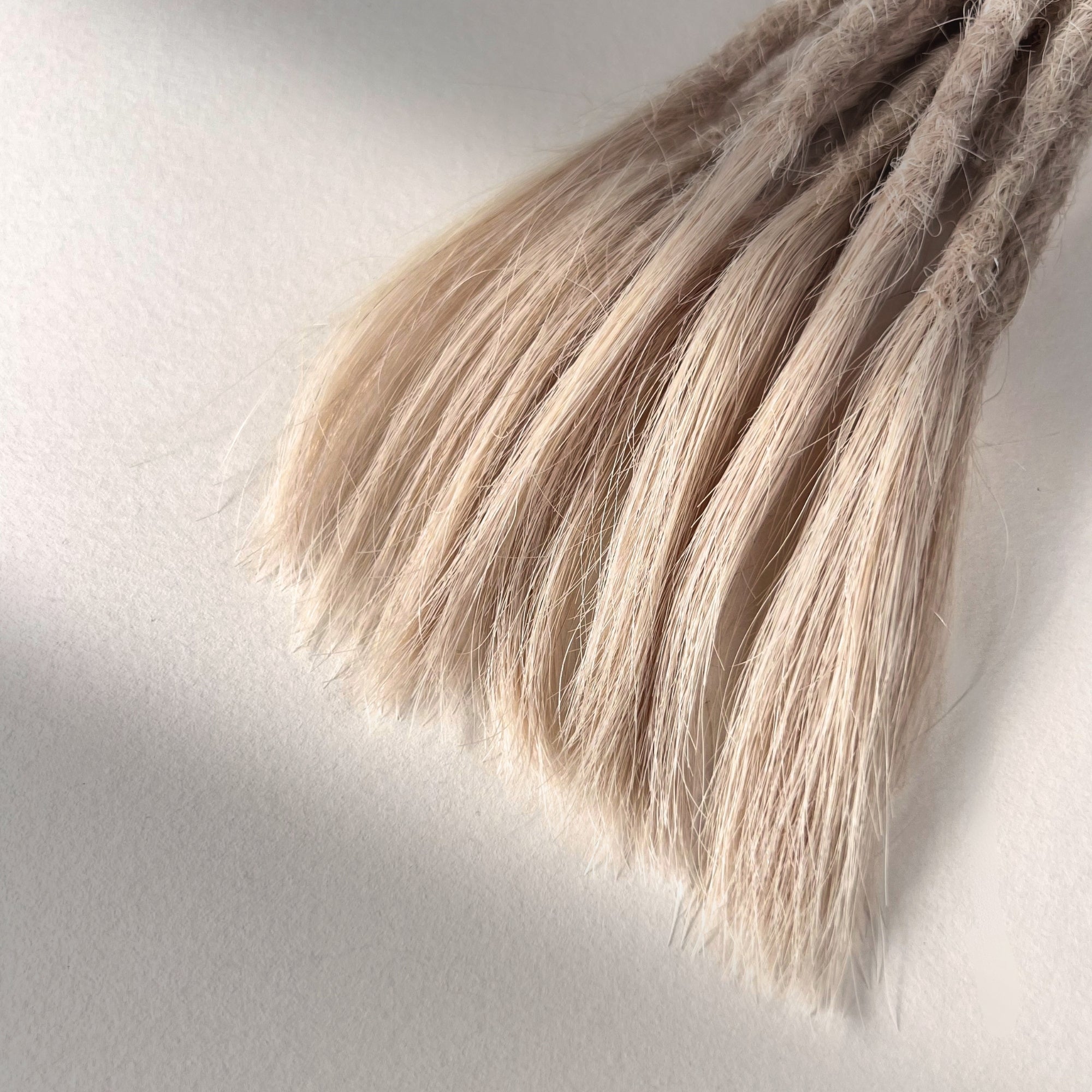 Tip detail of straight loc extensions with open ends in Cool Ash Blonde.