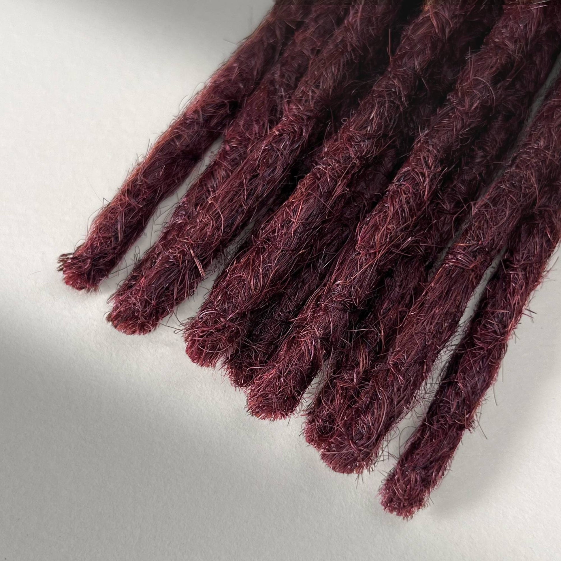 Tip detail of straight loc extensions with blunt ends in Rich Burgundy Red.