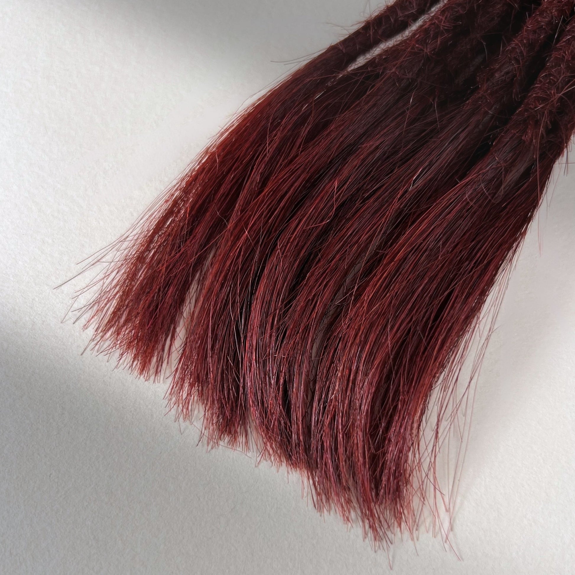 Tip detail of straight loc extensions with open ends in Rich Burgundy Red.