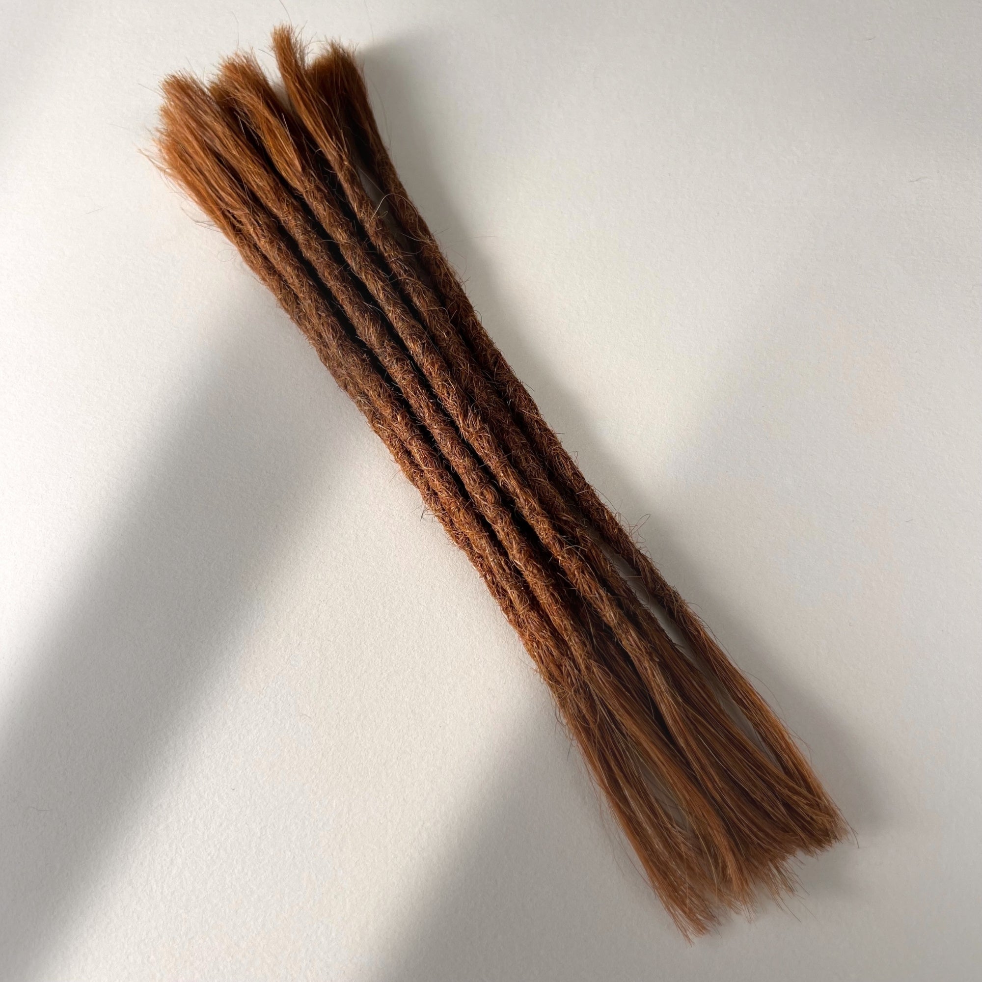 Full view of permanent straight loc extensions with open ends in Burnt Sienna Copper.