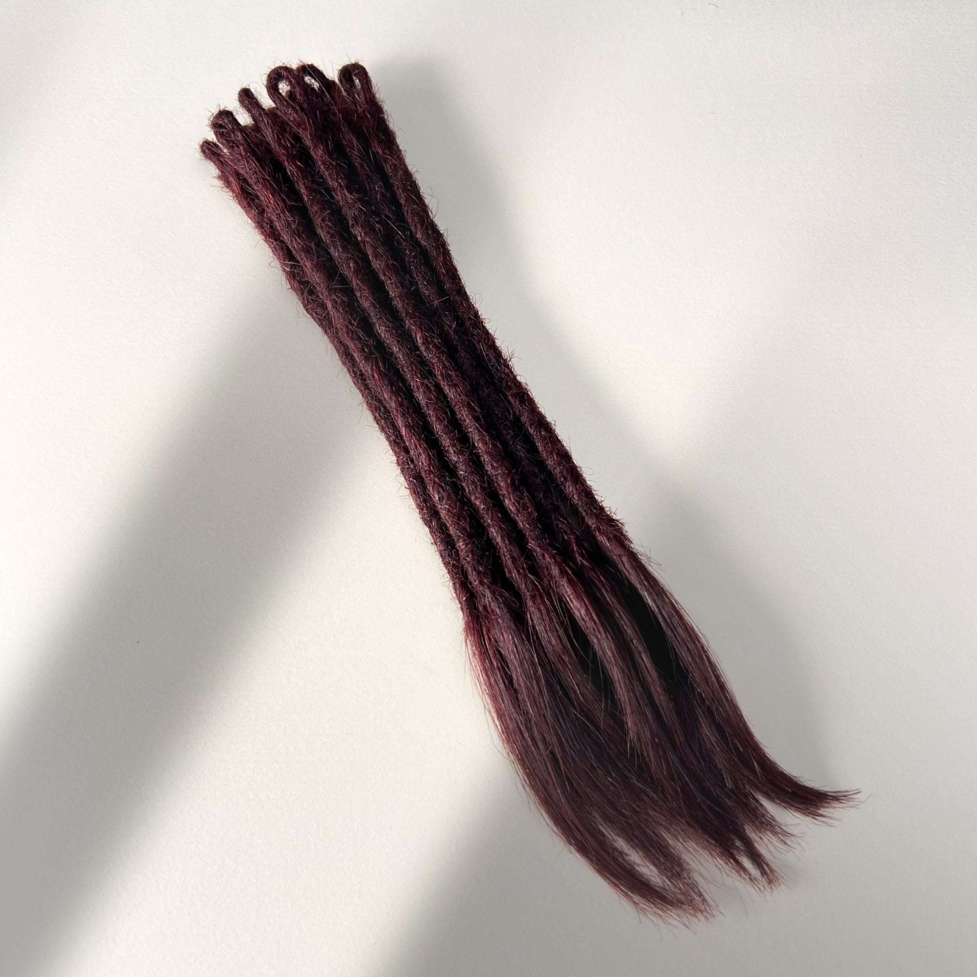 Full view of temporary single-ended straight loc extensions with open ends in Deep Crimson Red.