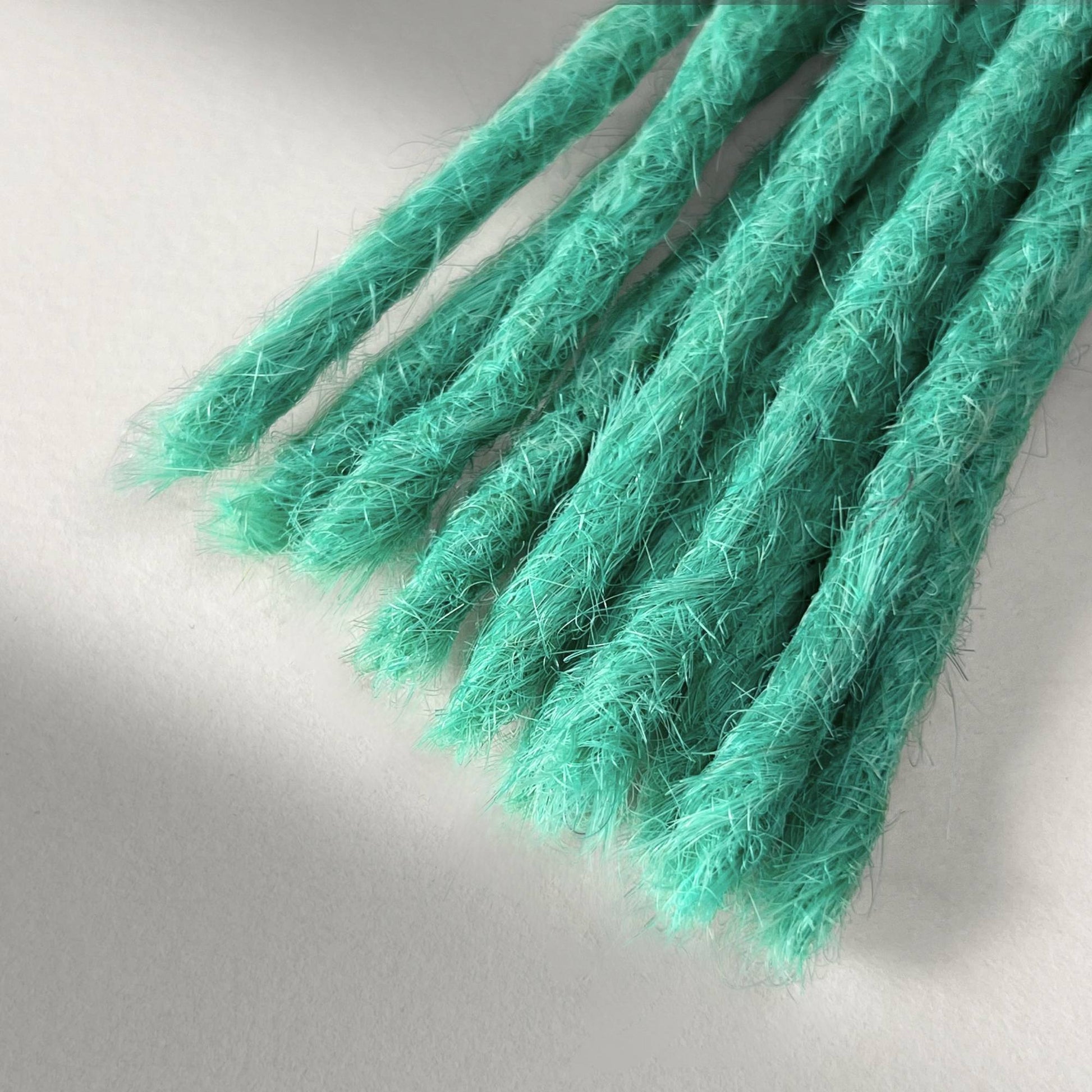 Tip detail of straight loc extensions with blunt ends in Pastel Emerald Green.