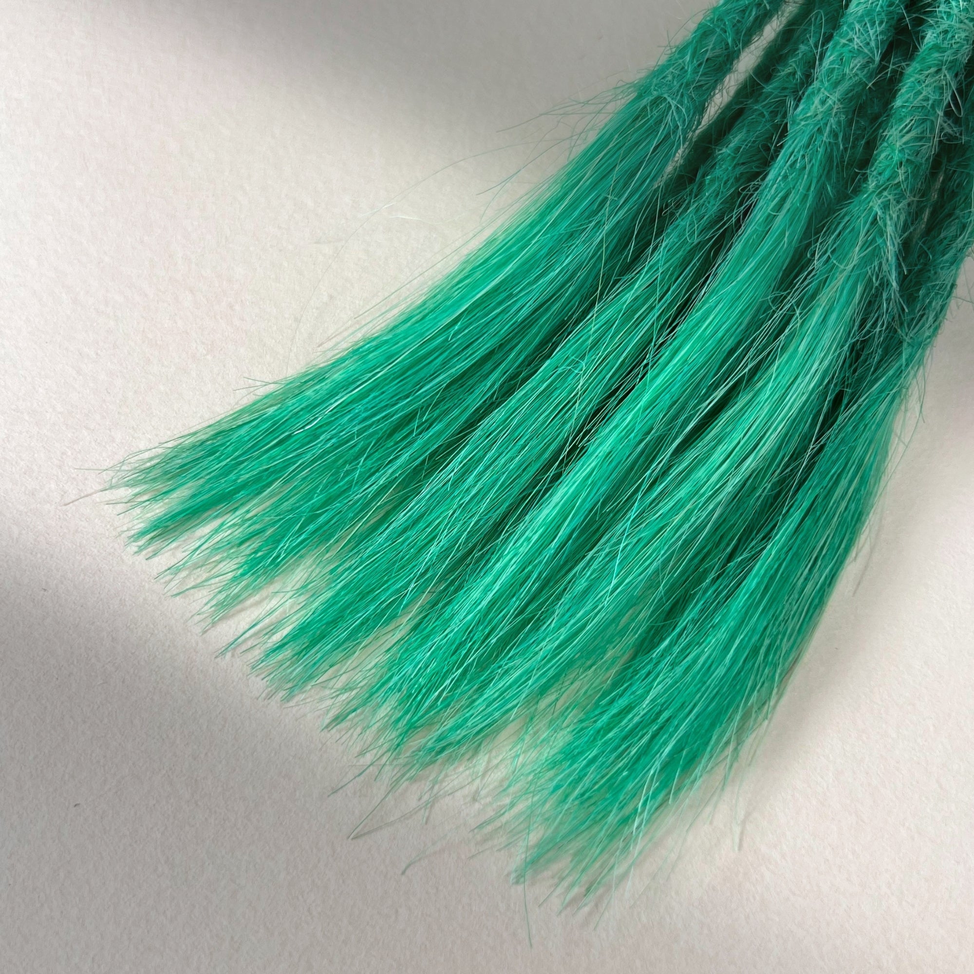 Tip detail of straight loc extensions with open ends in Pastel Emerald Green.