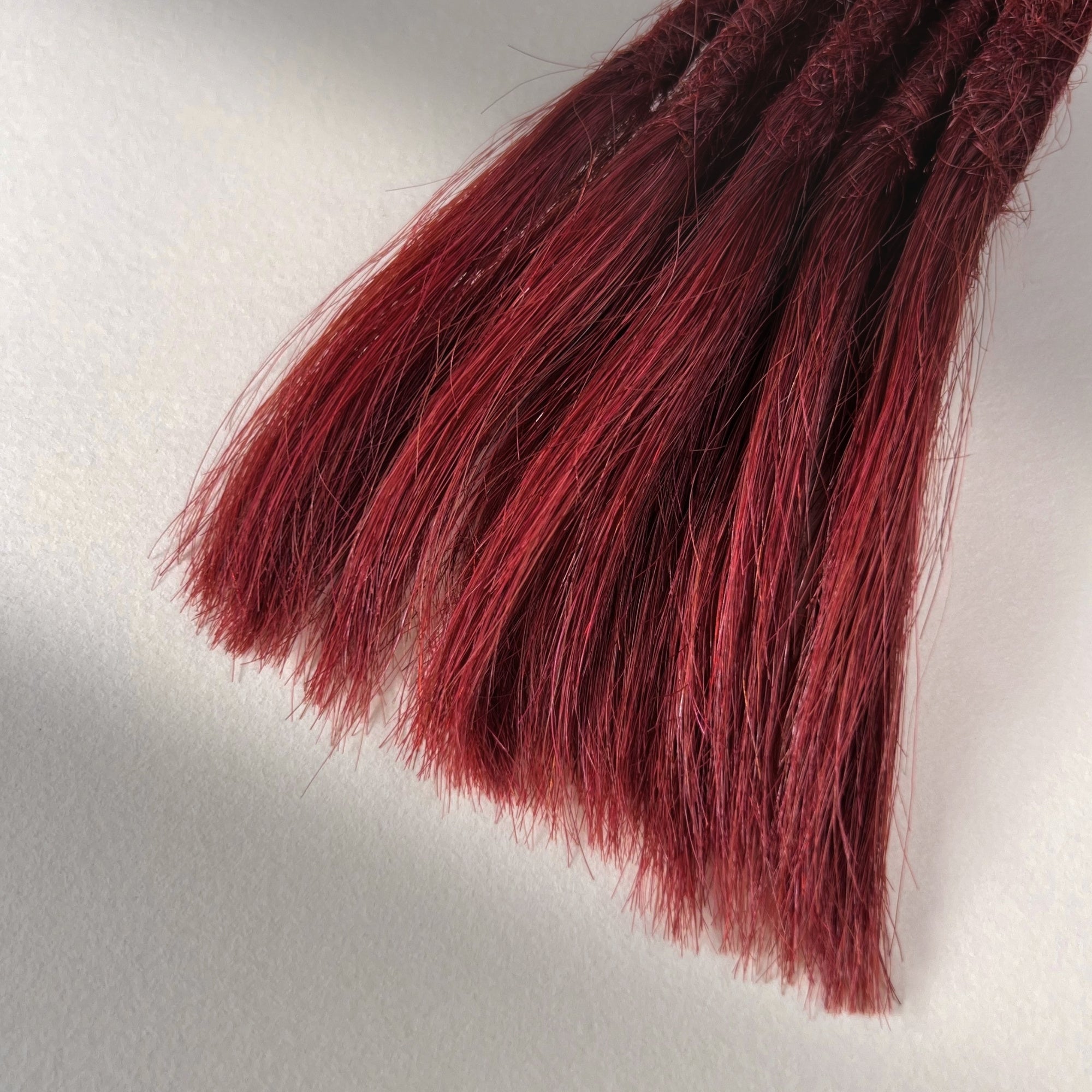 Tip detail of straight loc extensions with open ends in Deep Garnet Red.