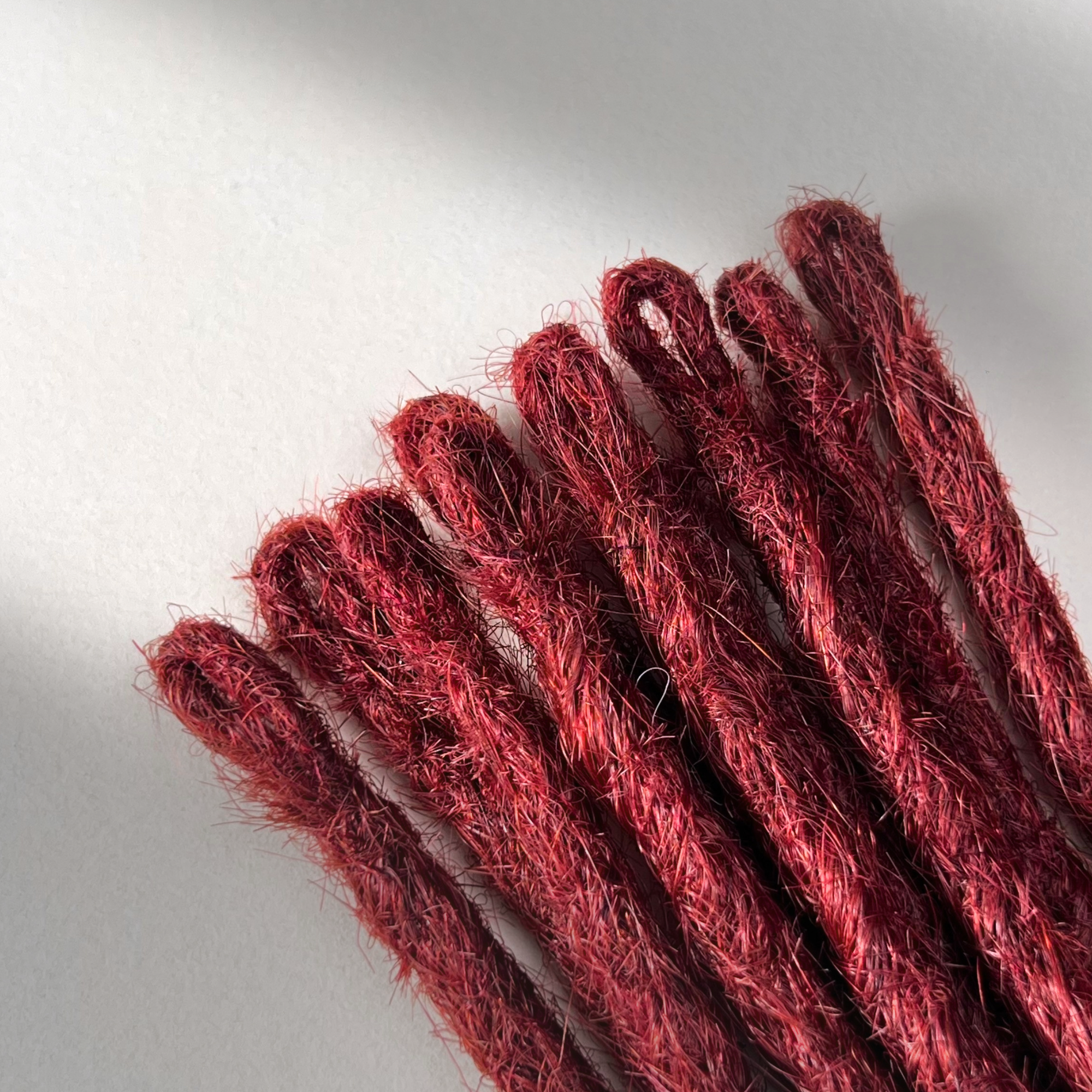 Loop detail of temporary single-ended straight loc extensions in Deep Garnet Red.