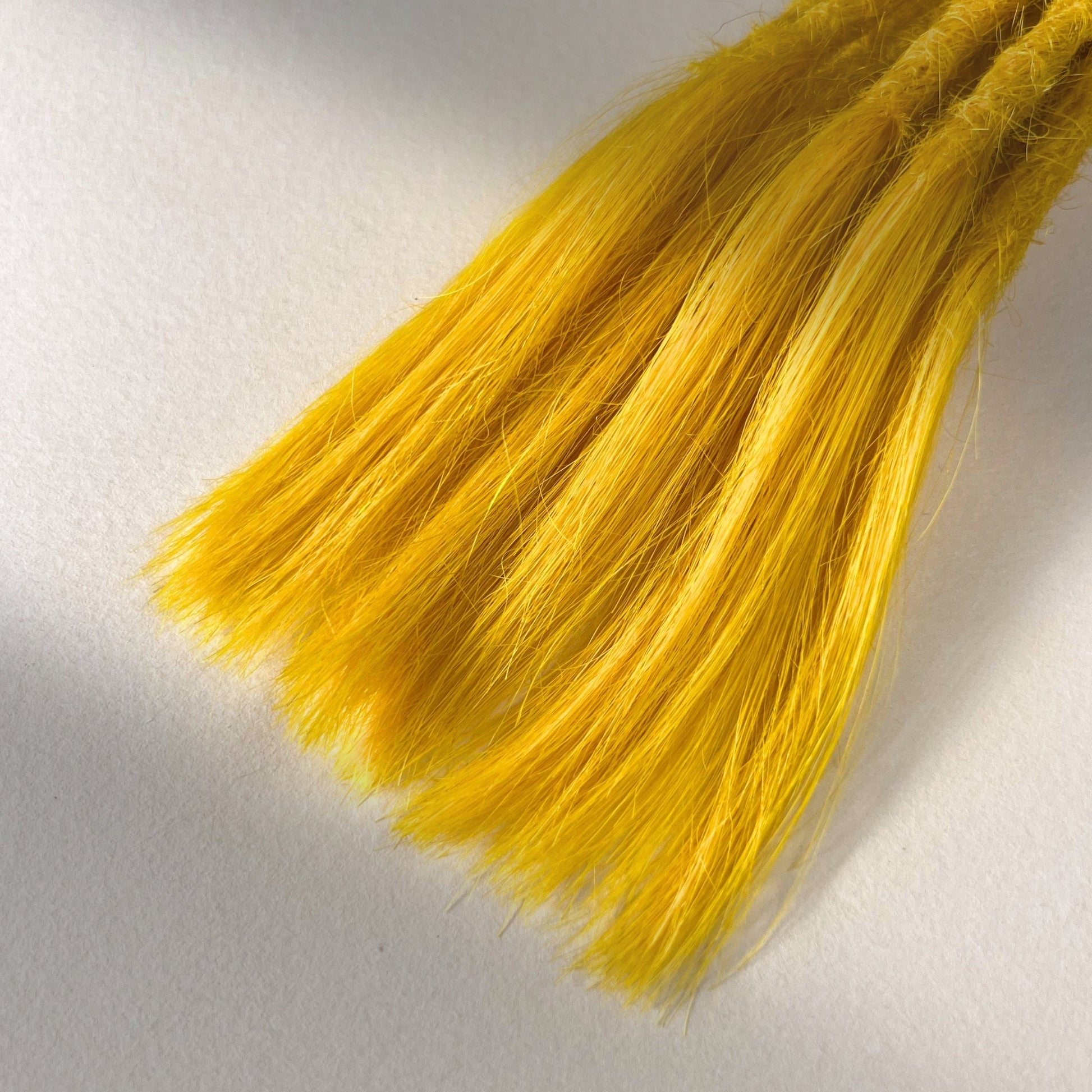 Tip detail of straight loc extensions with open ends in Lemon Yellow.