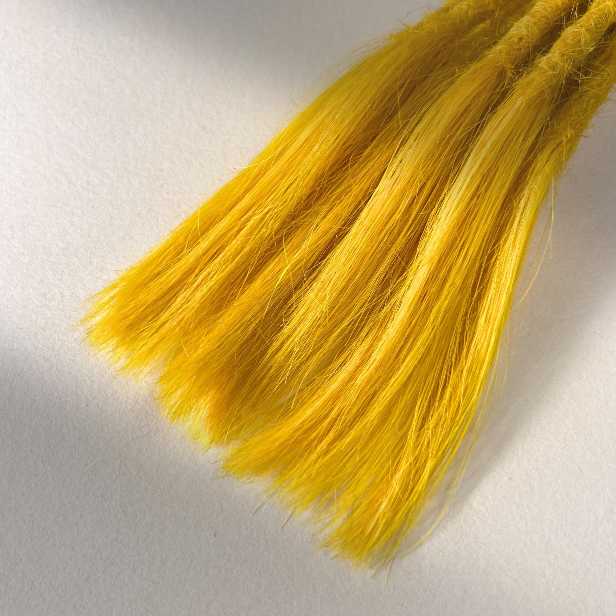 Tip detail of straight loc extensions with open ends in Lemon Yellow.