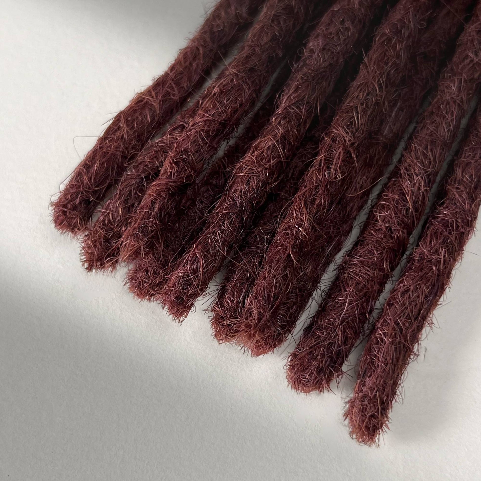 Tip detail of straight loc extensions with blunt ends in Warm Mahogany Red.
