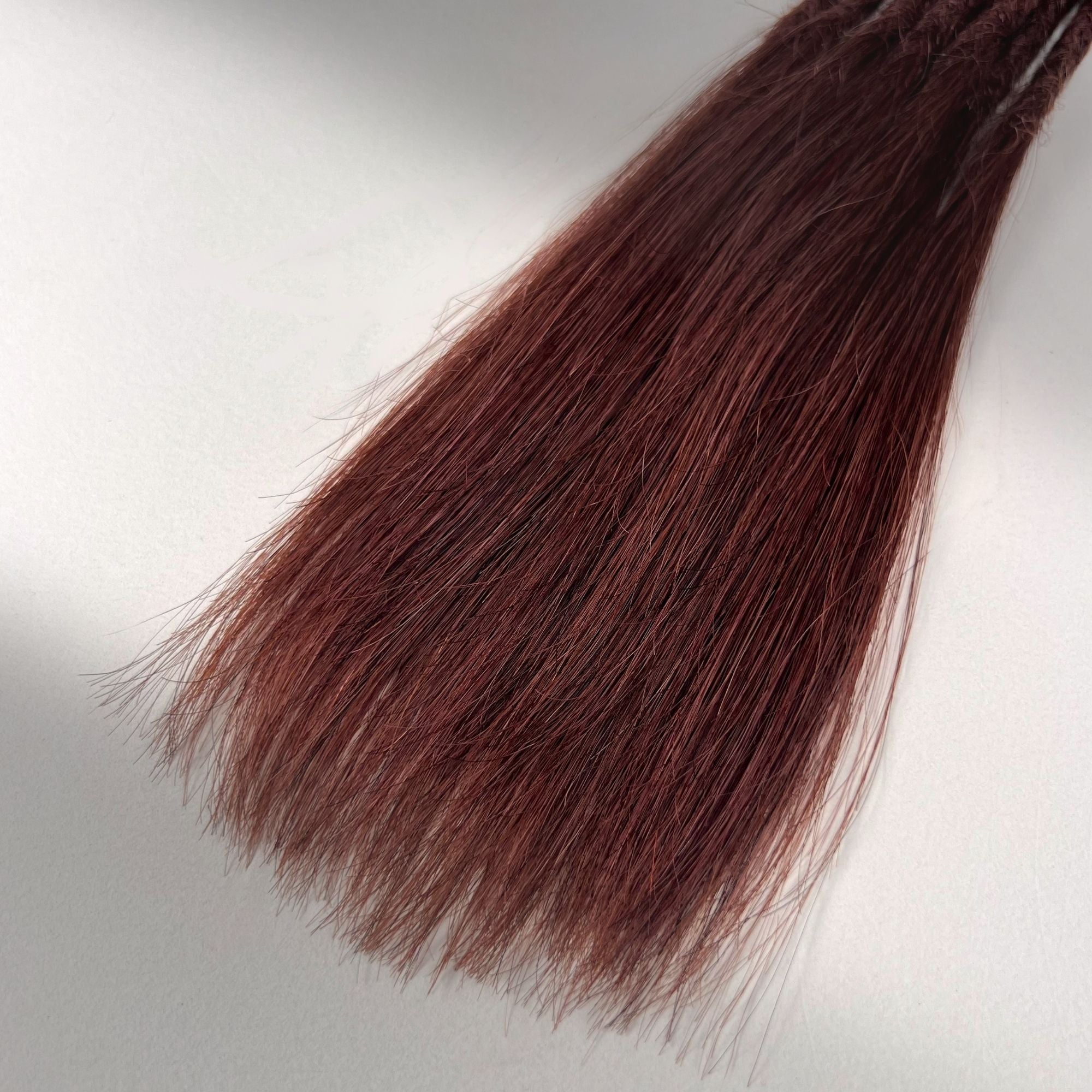Tip detail of straight loc extensions with long loose ends in Warm Mahogany Red.