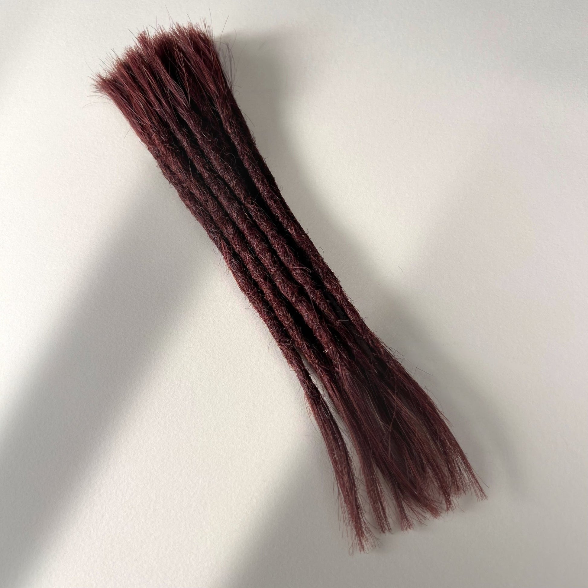 Full view of permanent straight loc extensions with open ends in Warm Mahogany Red.