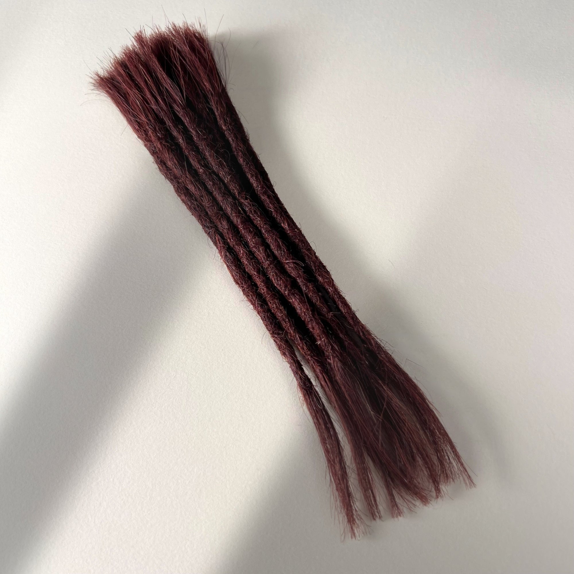Full view of permanent straight loc extensions with open ends in Warm Mahogany Red.