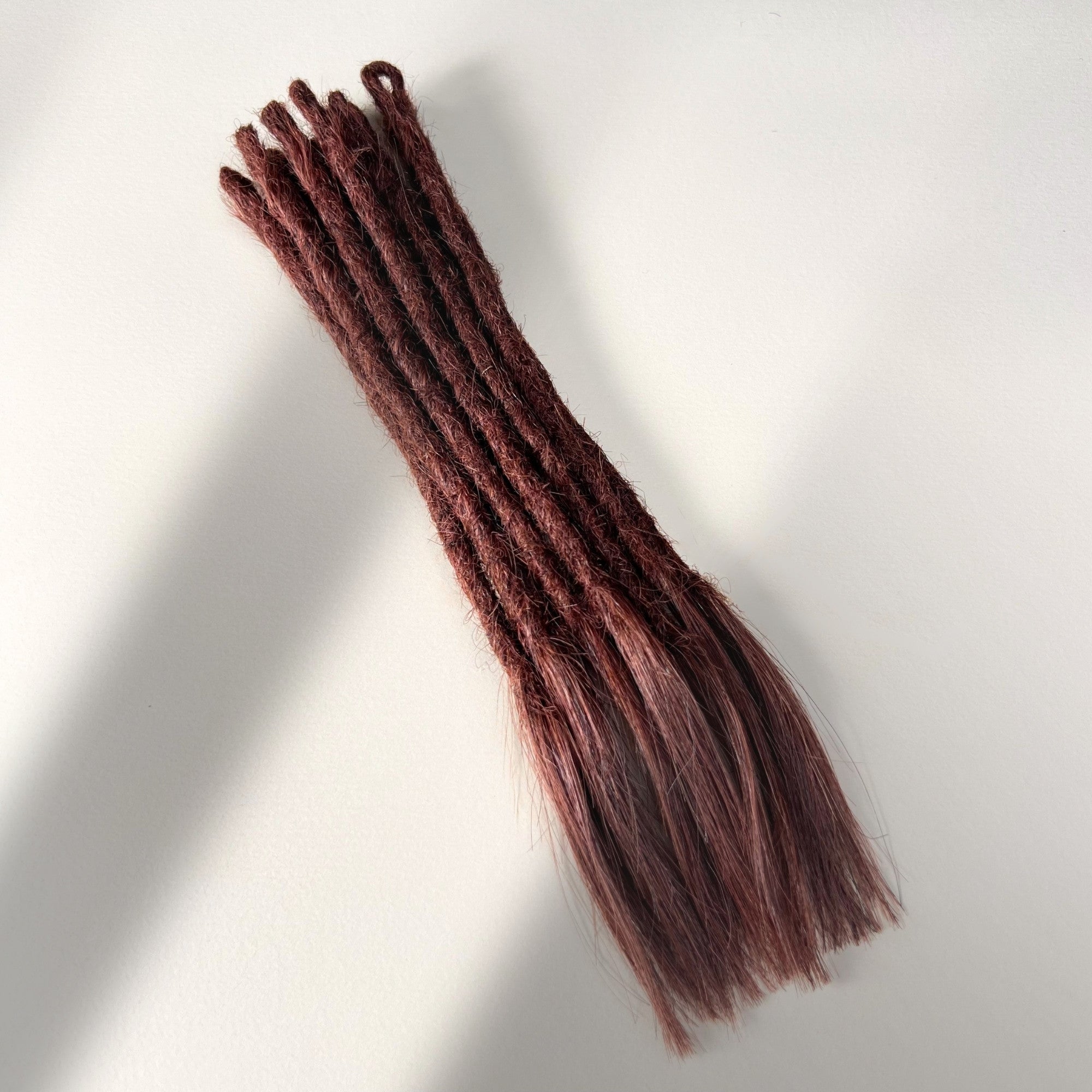 Full view of temporary single-ended straight loc extensions with open ends in Warm Mahogany Red.