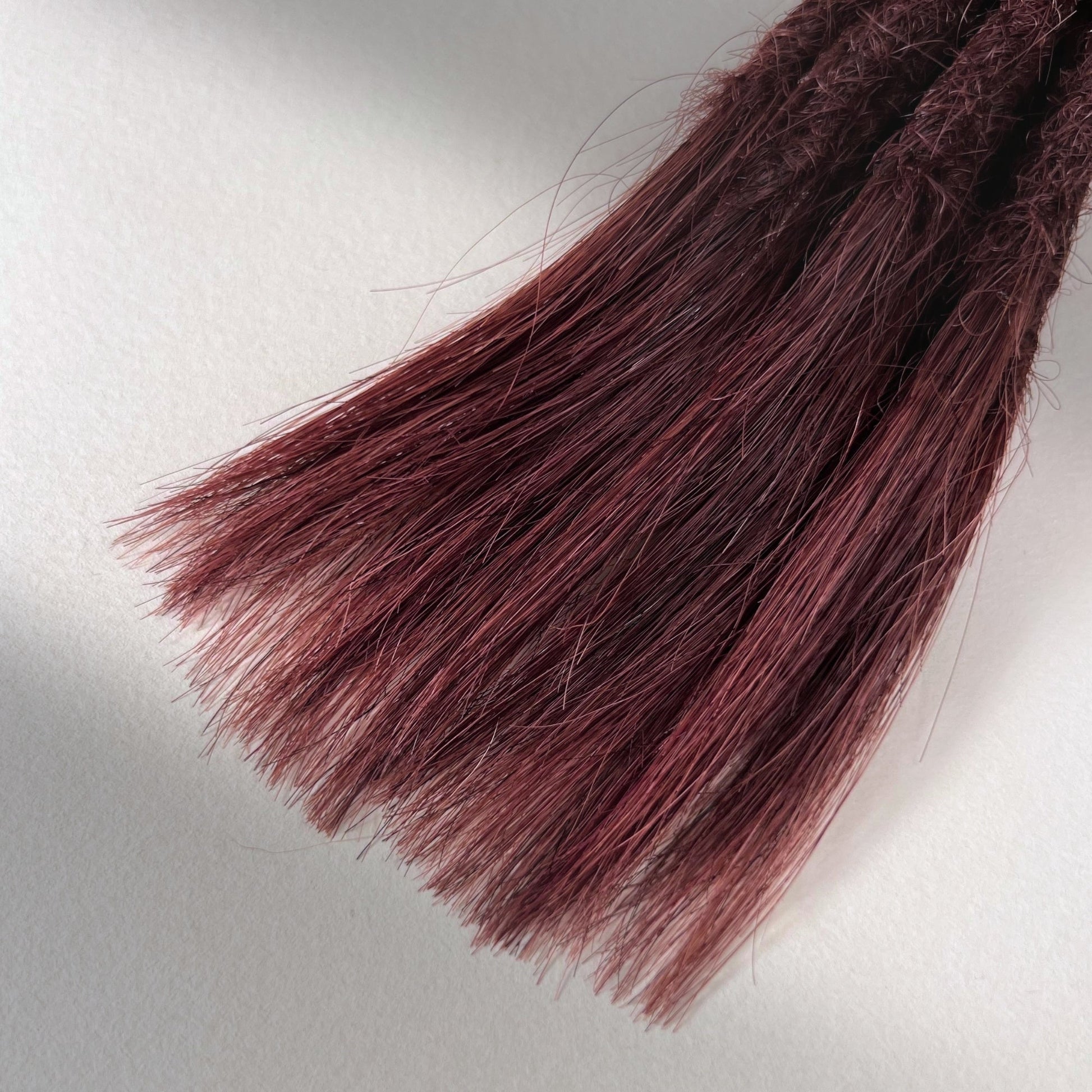 Tip detail of straight loc extensions with open ends in Warm Mahogany Red.