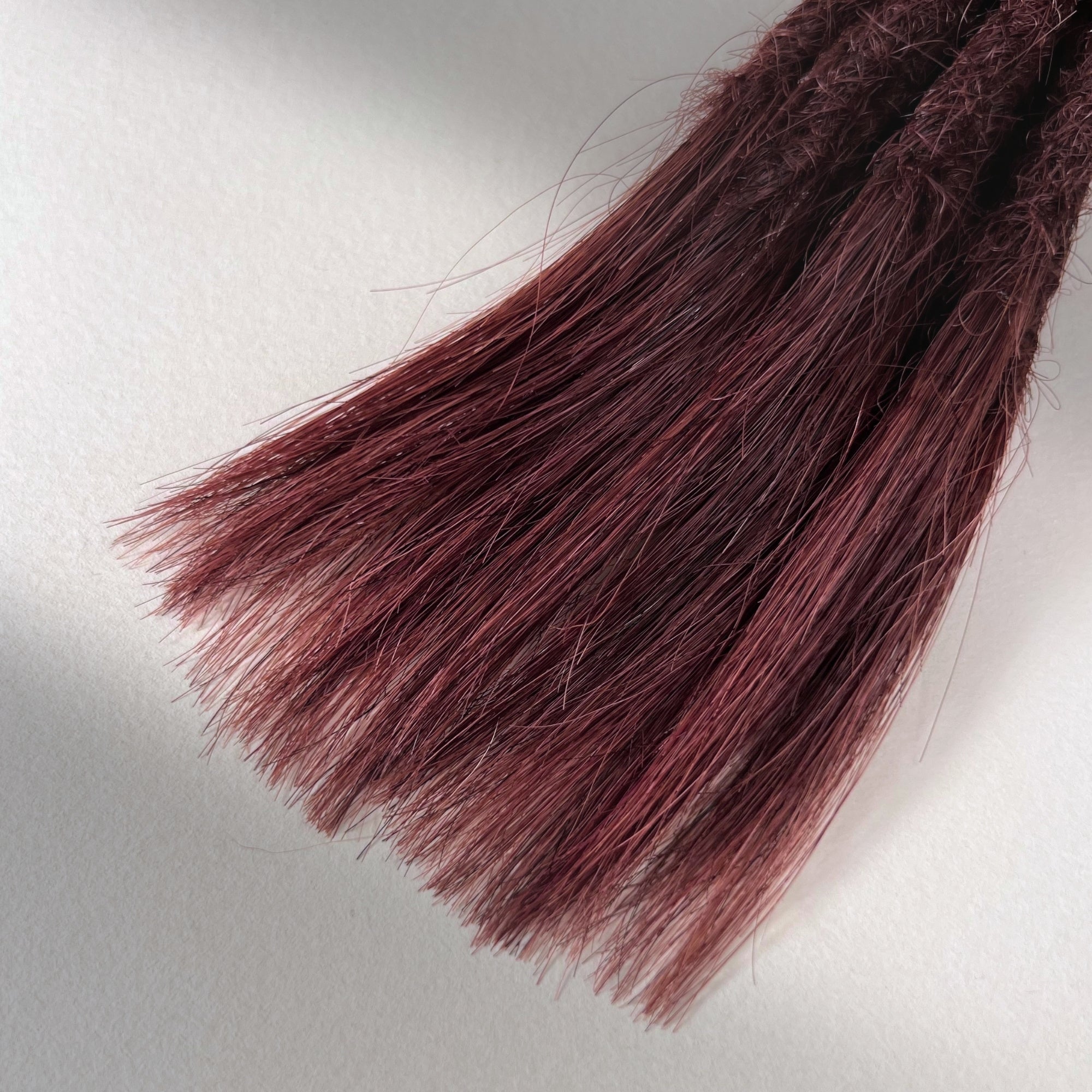 Tip detail of straight loc extensions with open ends in Warm Mahogany Red.