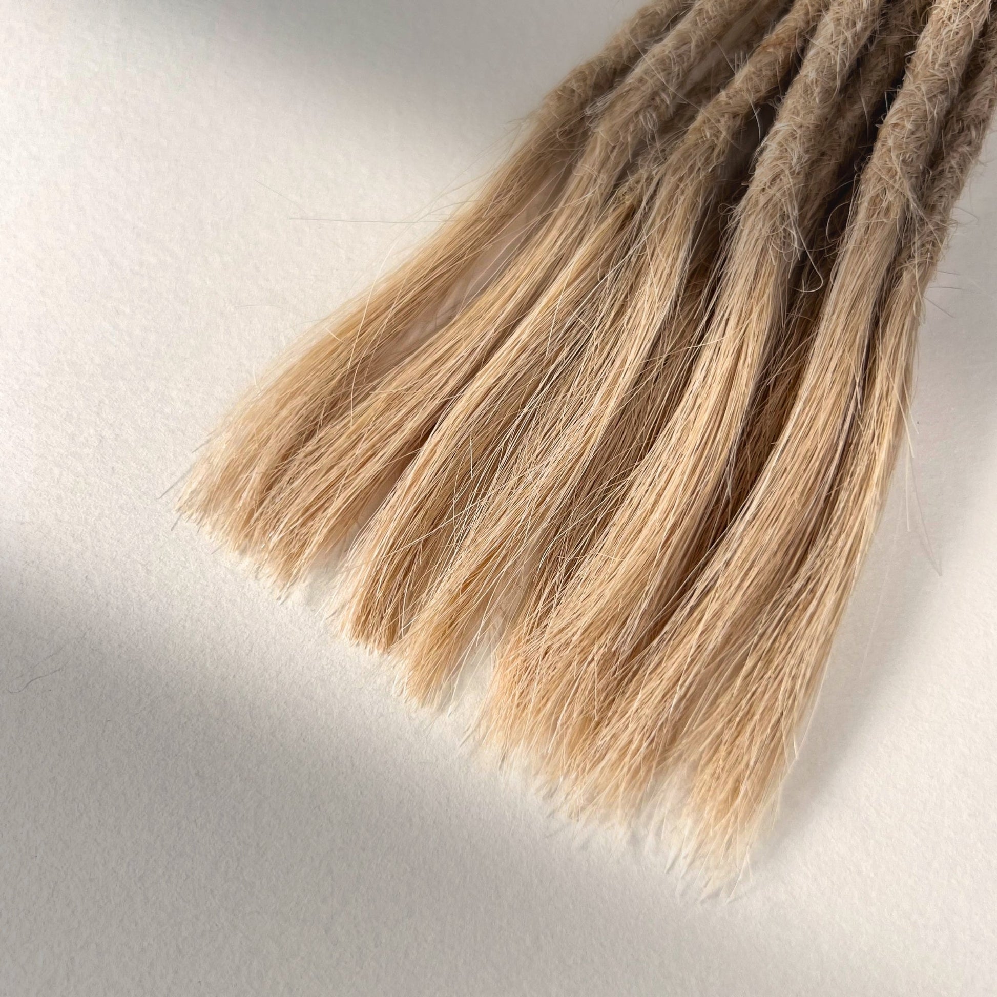 Tip detail of straight loc extensions with open ends in Vanilla Blonde.