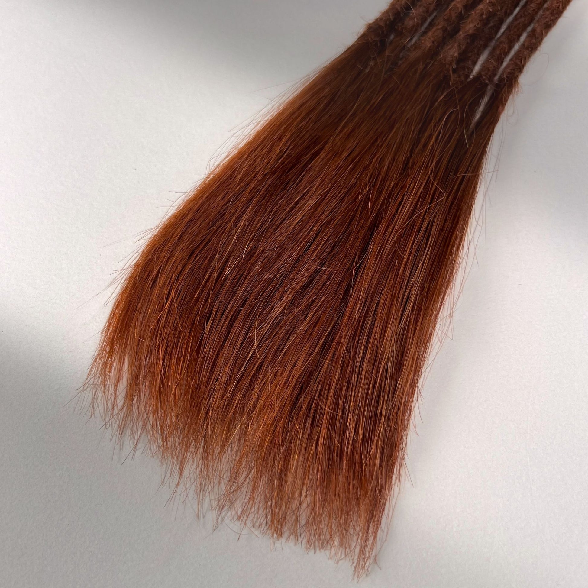 Tip detail of straight loc extensions with long loose ends in Warm Maple Copper.