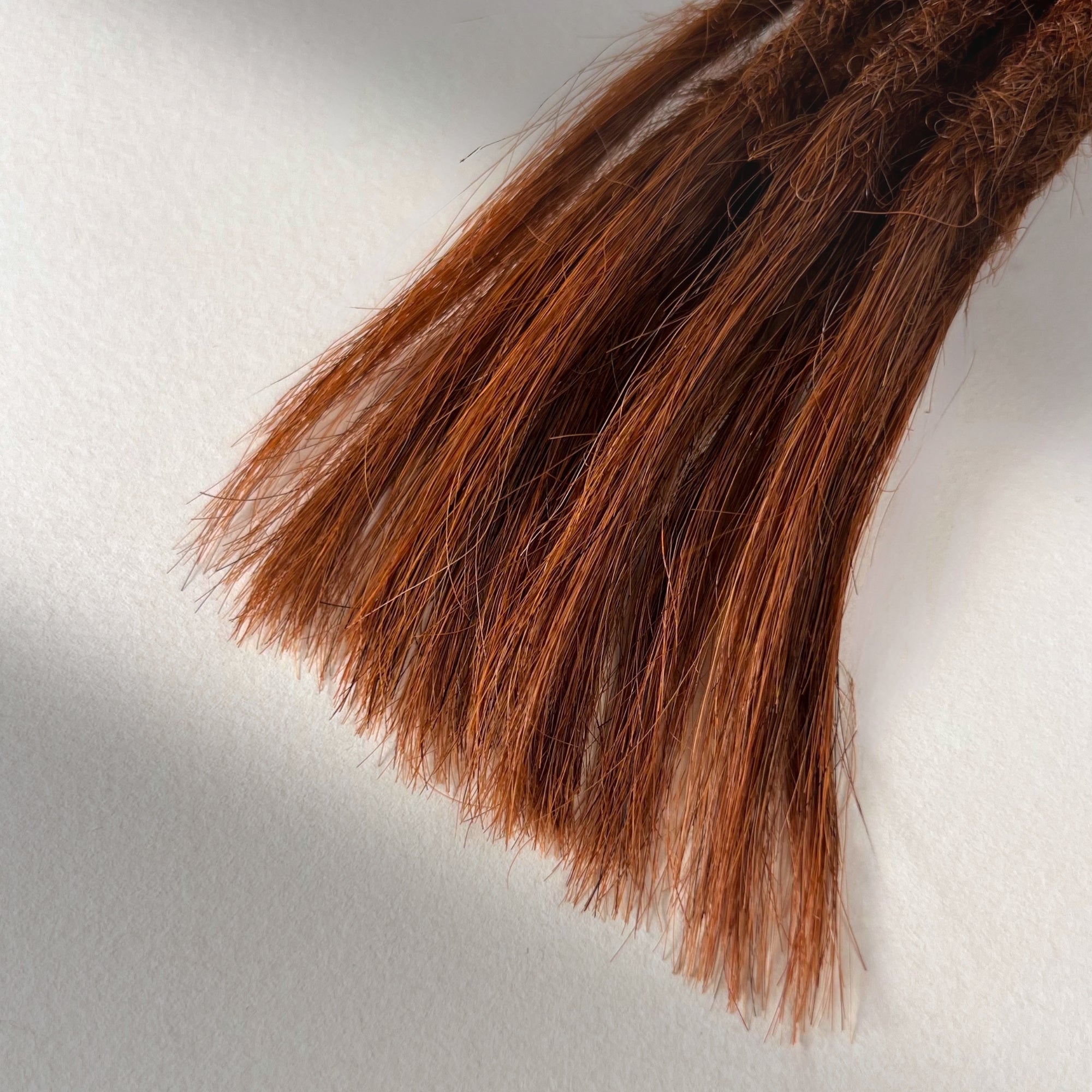 Tip detail of straight loc extensions with open ends in Warm Maple Copper.