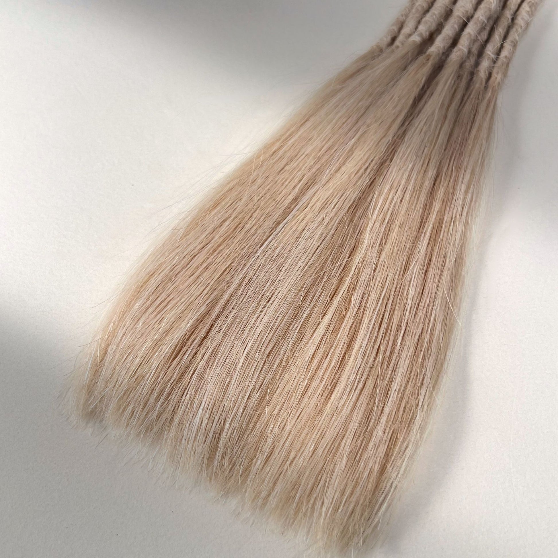 Tip detail of straight loc extensions with long loose ends in Soft Rose Blonde.
