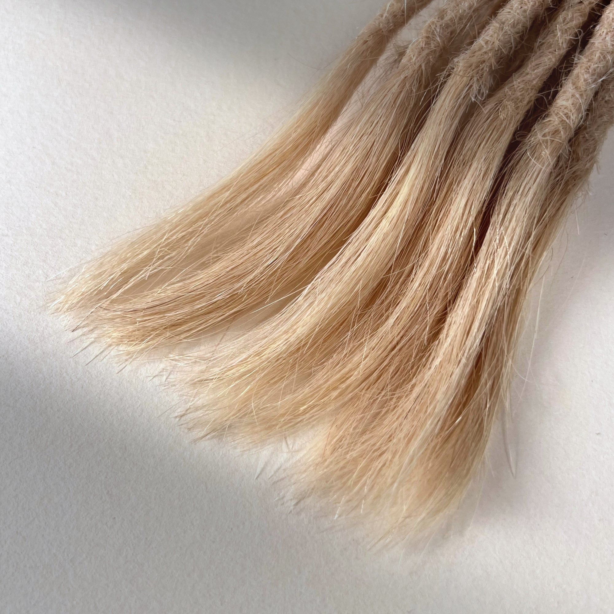 Tip detail of straight loc extensions with open ends in Soft Rose Blonde.