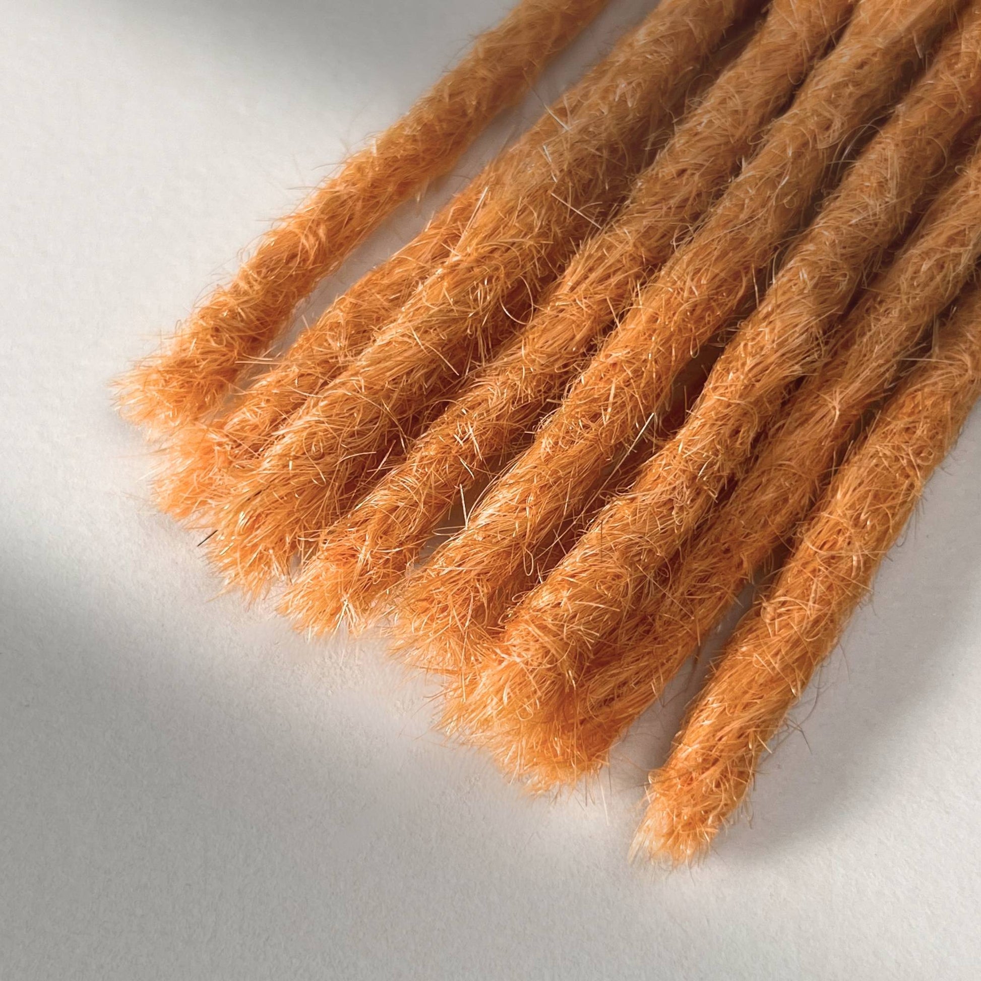Tip detail of straight loc extensions with blunt ends in Peach Orange.