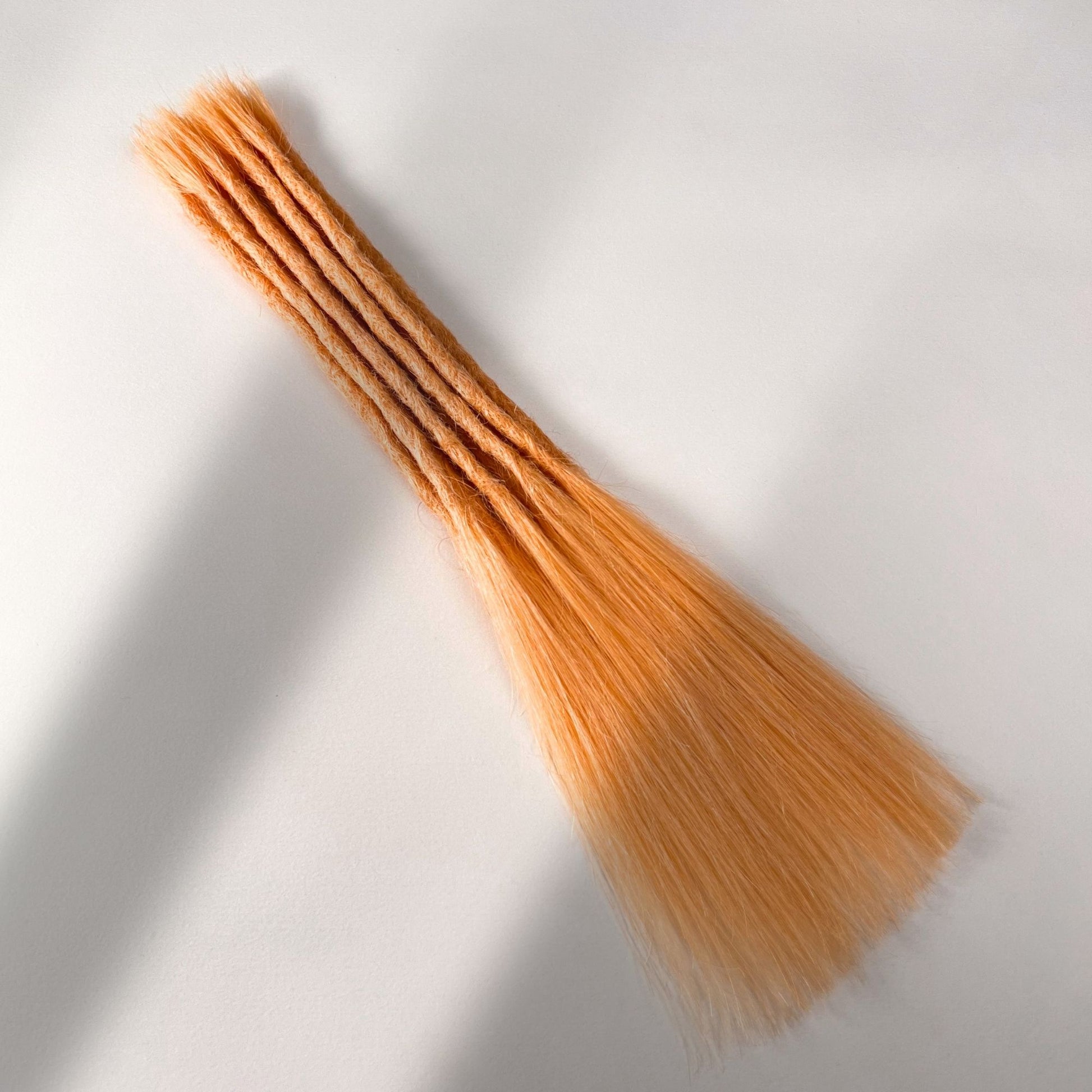 Full view of permanent straight loc extensions with long loose ends in Peach Orange.