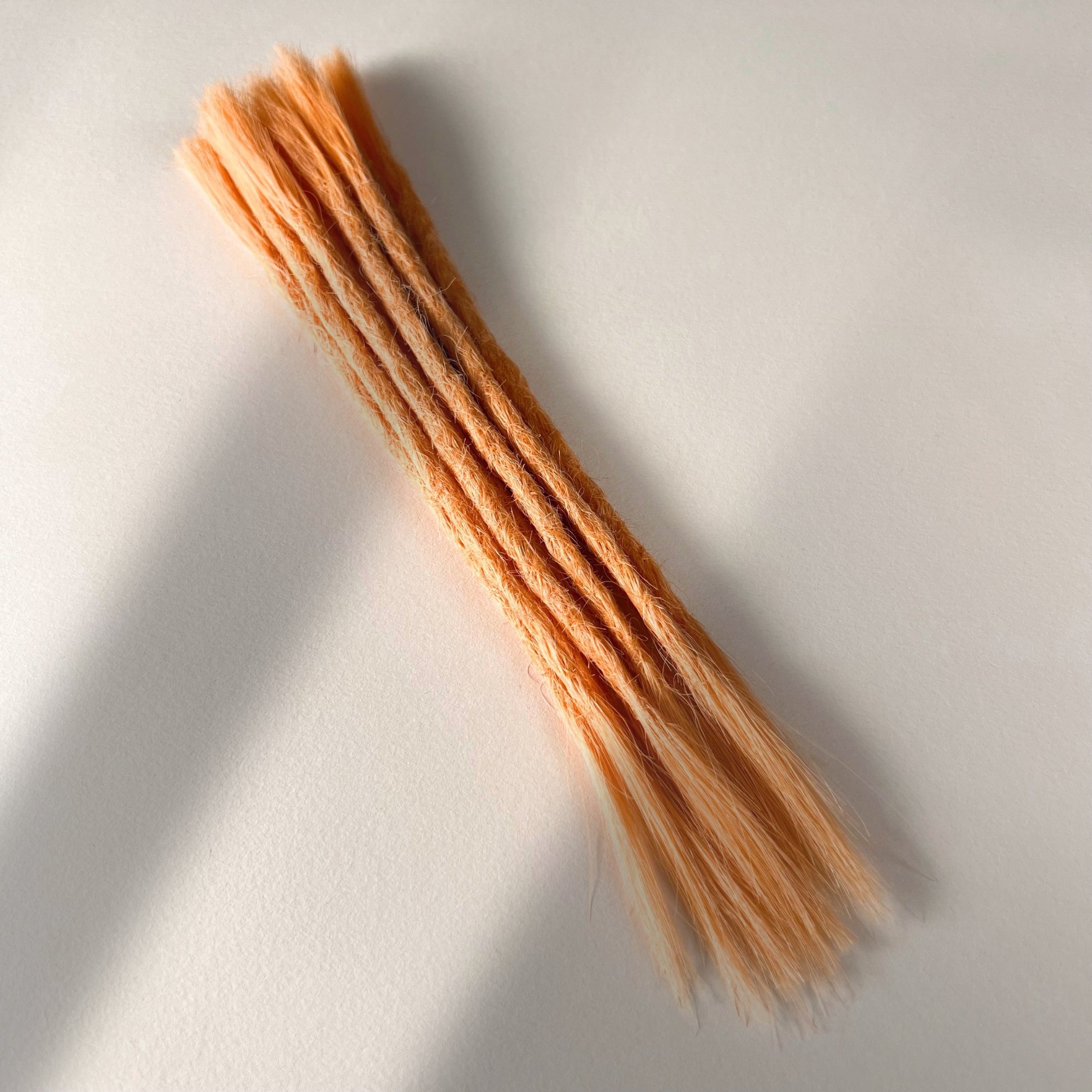 Full view of permanent straight loc extensions with open ends in Peach Orange.