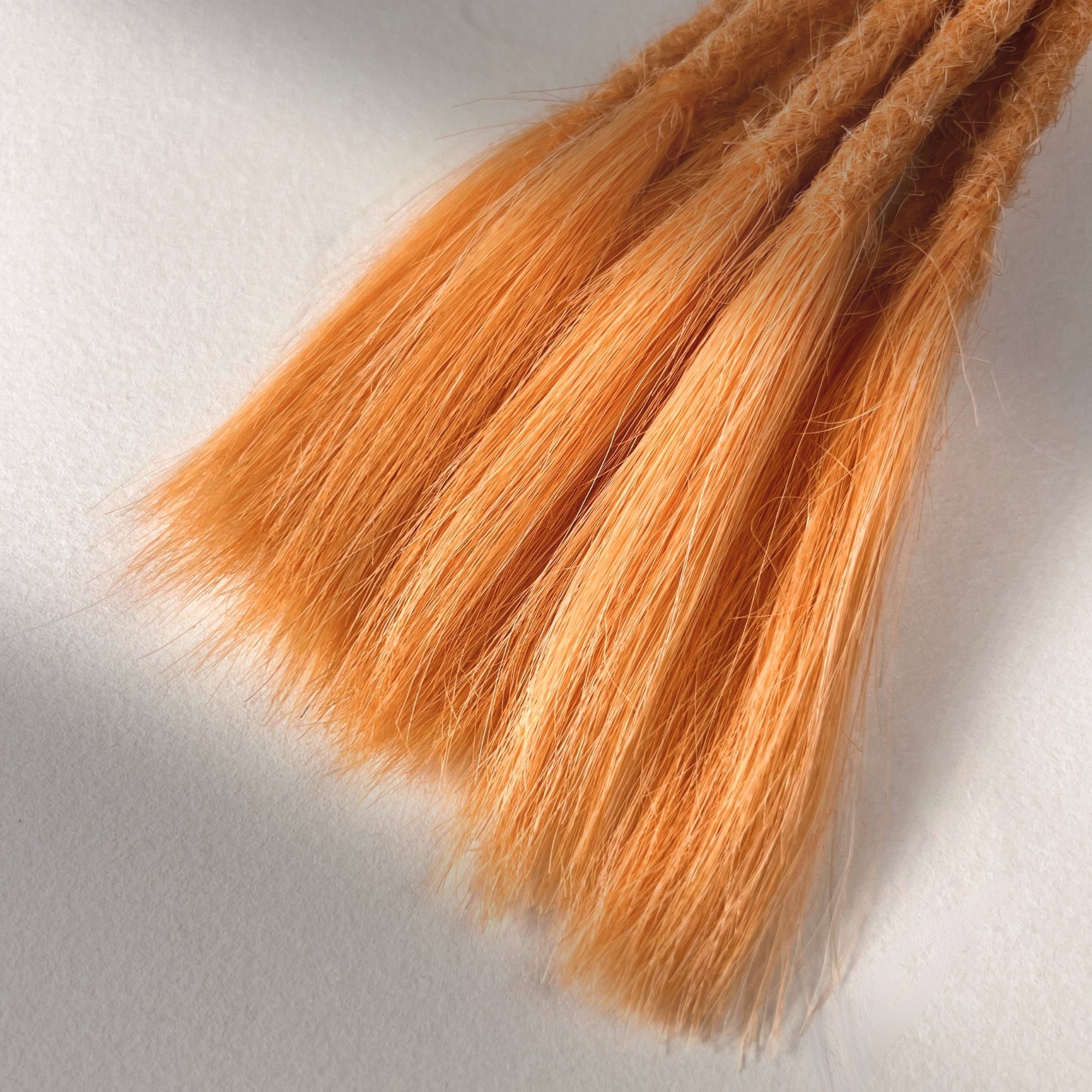 Tip detail of straight loc extensions with open ends in Peach Orange.