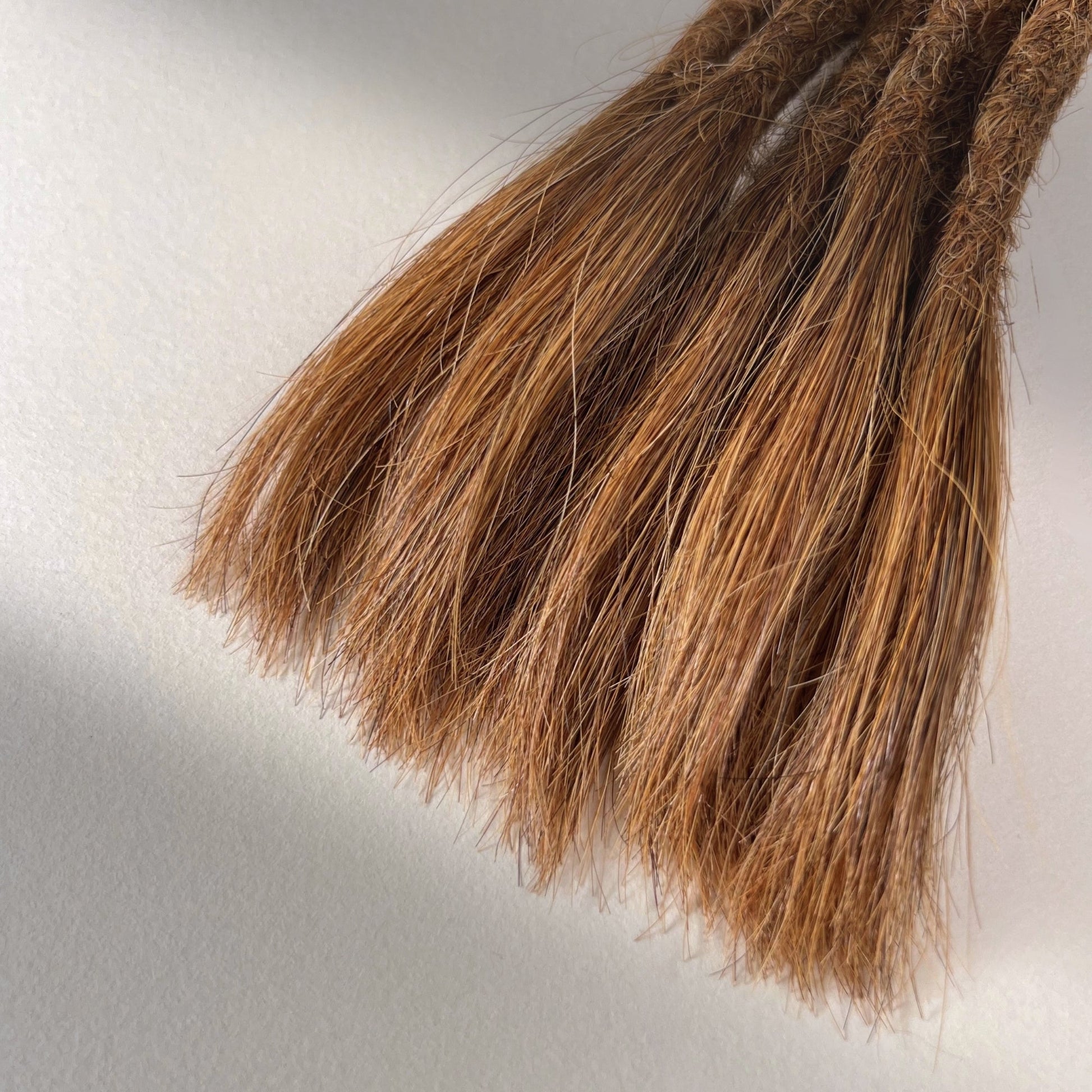 Tip detail of straight loc extensions with open ends in Auburn Copper.