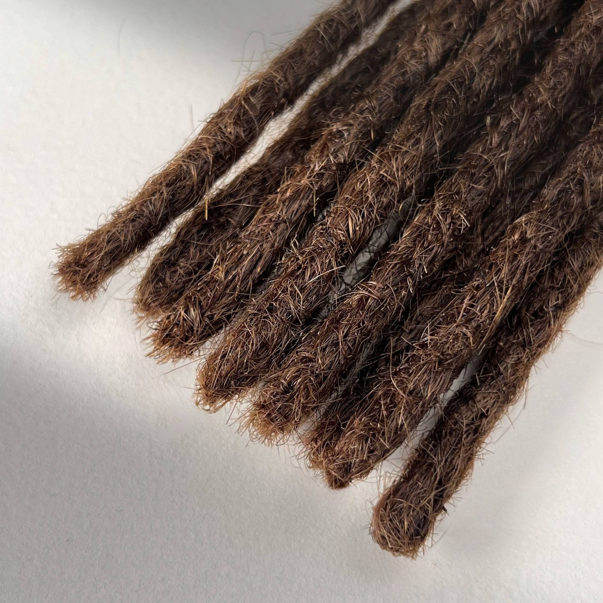 Tip detail of straight loc extensions with blunt ends in Warm Cinnamon Brown.