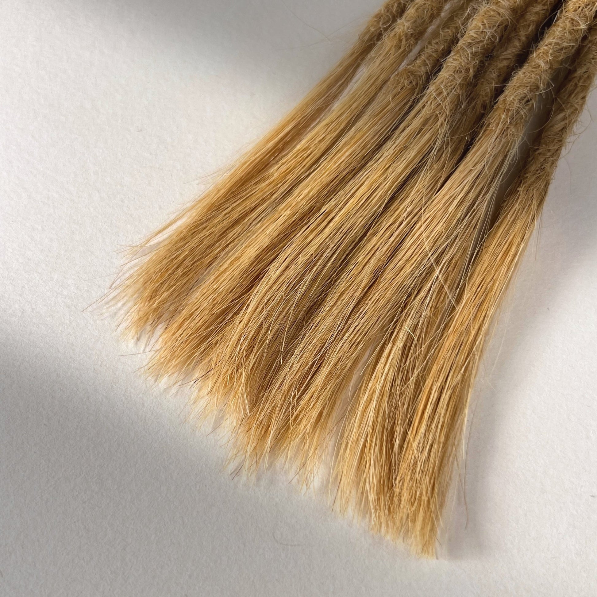 Tip detail of straight loc extensions with open ends in Sunkissed Blonde.