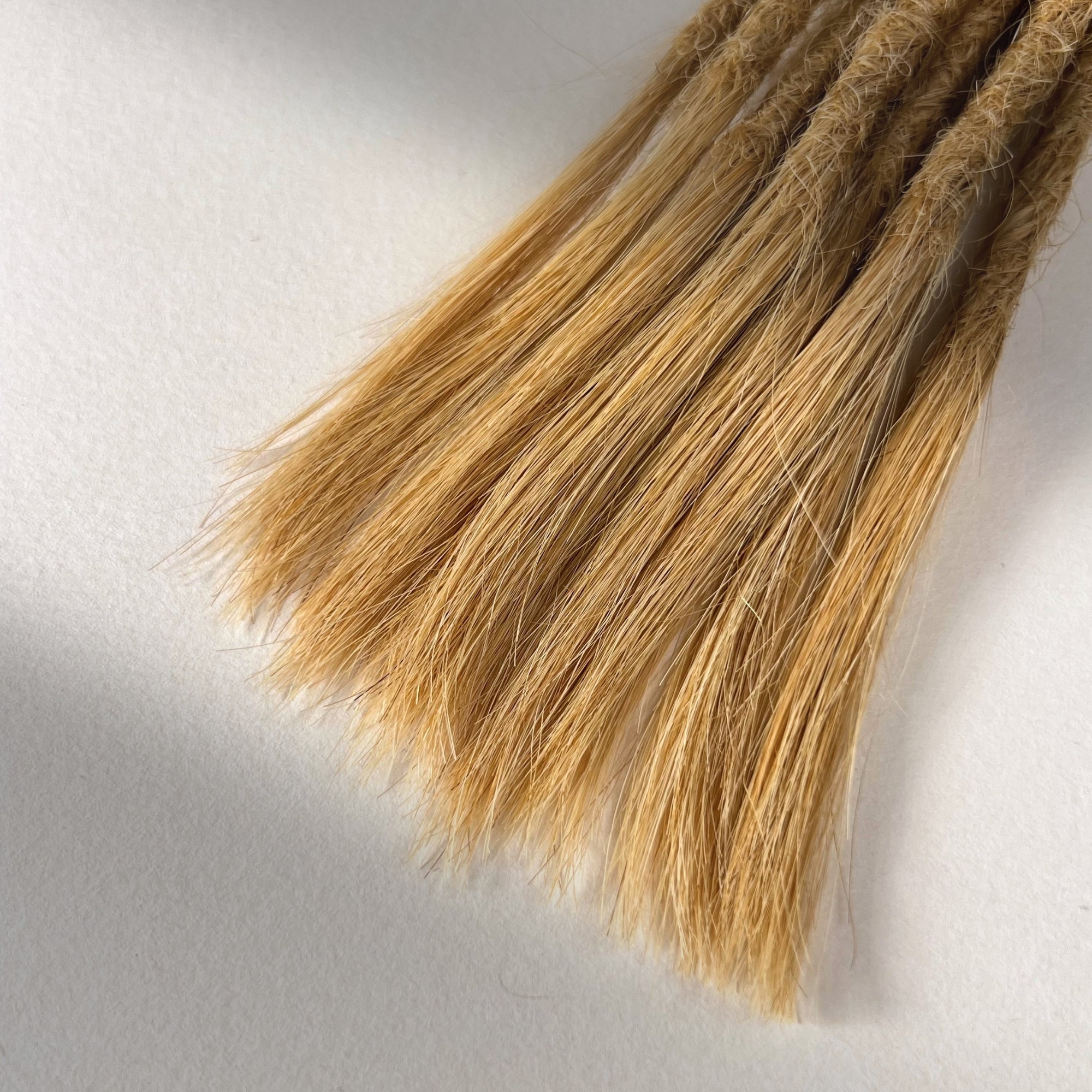Tip detail of straight loc extensions with open ends in Sunkissed Blonde.