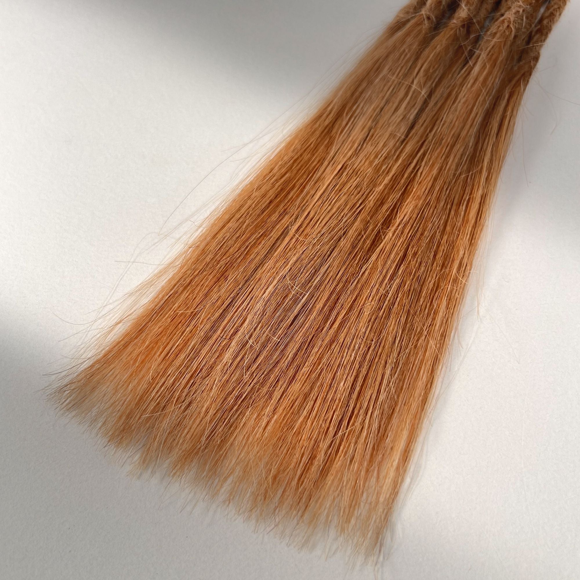 Tip detail of straight loc extensions with long loose ends in Warm Copper Blonde.