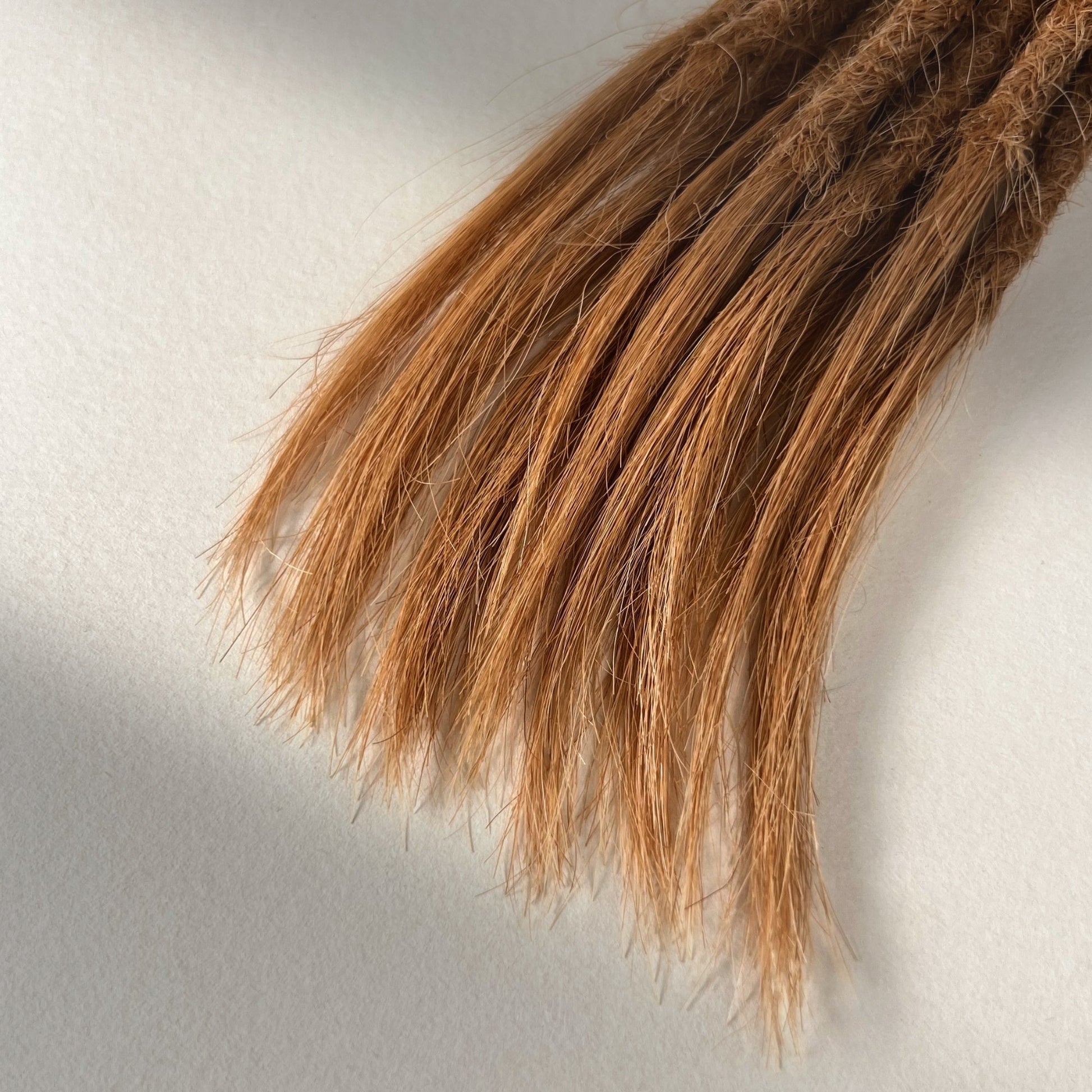 Tip detail of straight loc extensions with open ends in Warm Copper Blonde.
