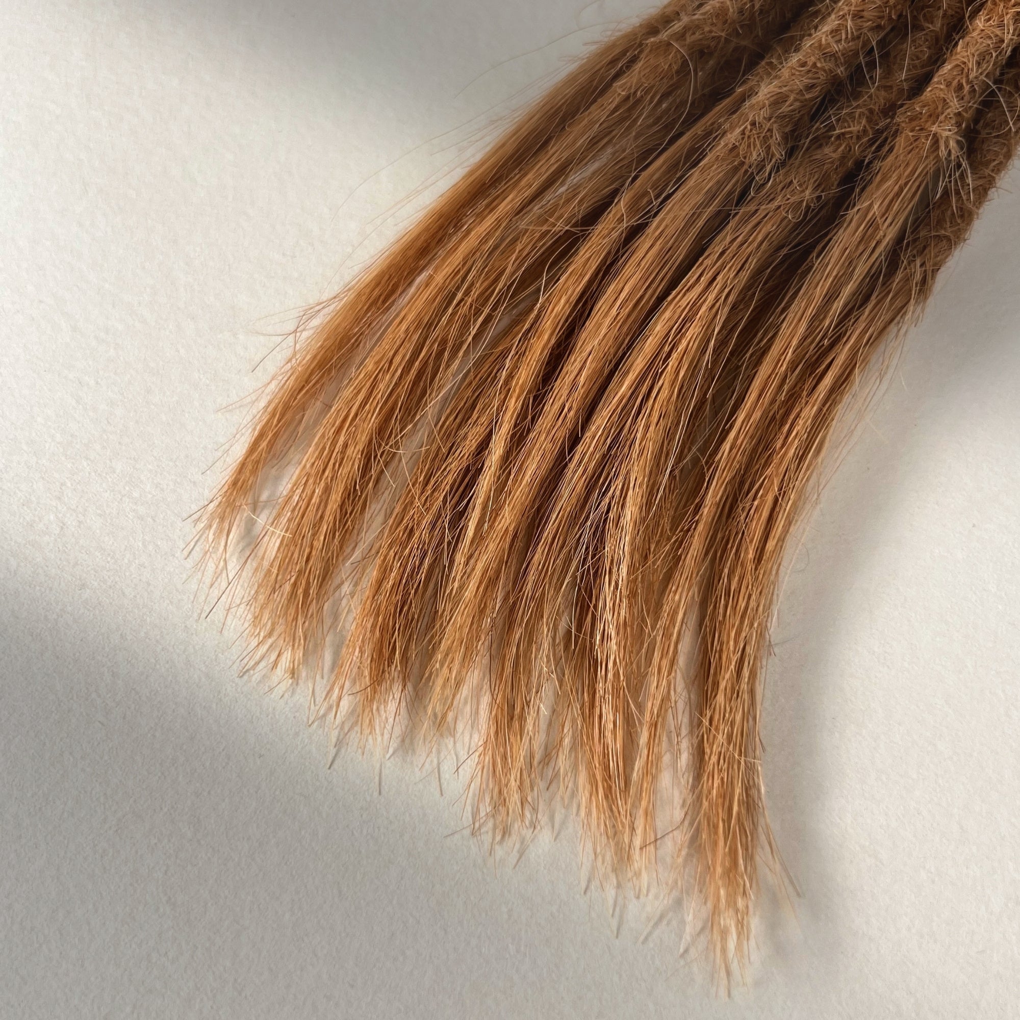 Tip detail of straight loc extensions with open ends in Warm Copper Blonde.